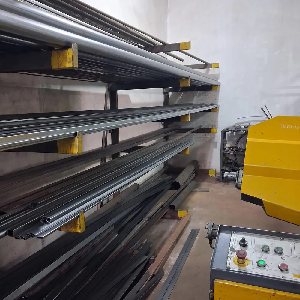 Racked steel stock in the workshop &mdash; square tube, angle, flat bar and rod, sorted by profile