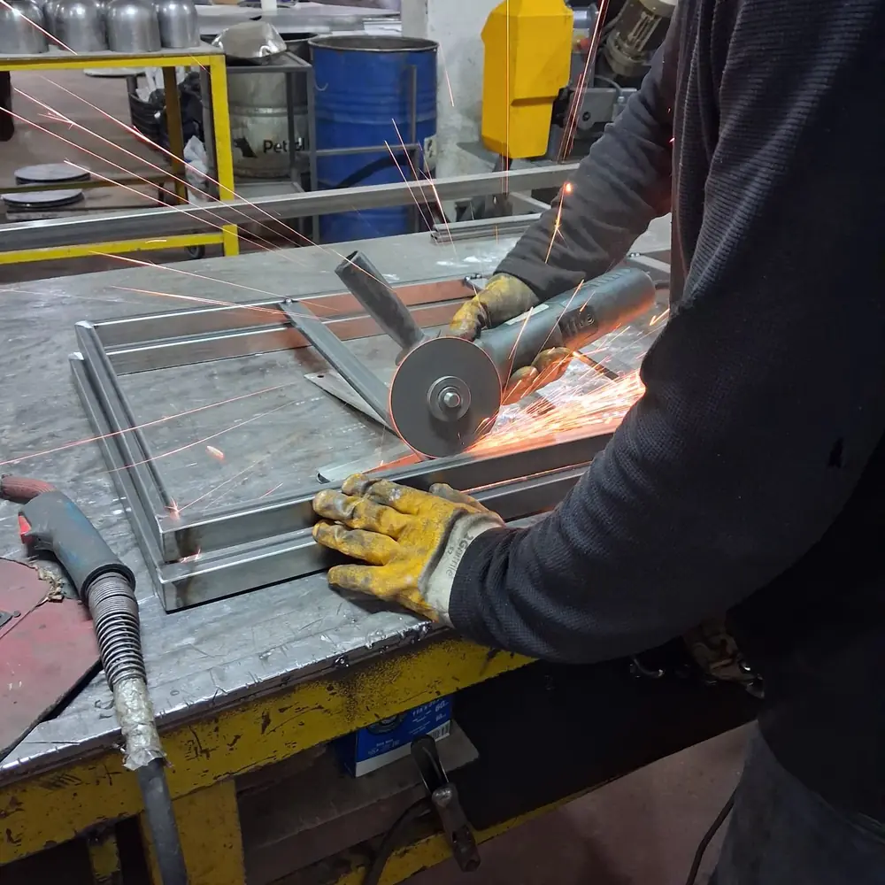 Angle grinder dressing a cut on a steel mirror frame on the bench, sparks flying