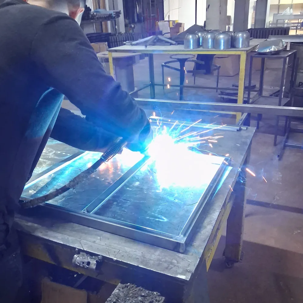 MIG welding a steel mirror frame flat on the bench, arc and sparks