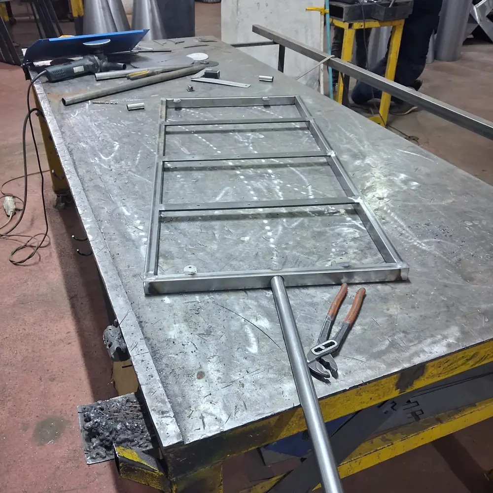 A welded steel mirror frame squared up on the bench with a length of rod alongside